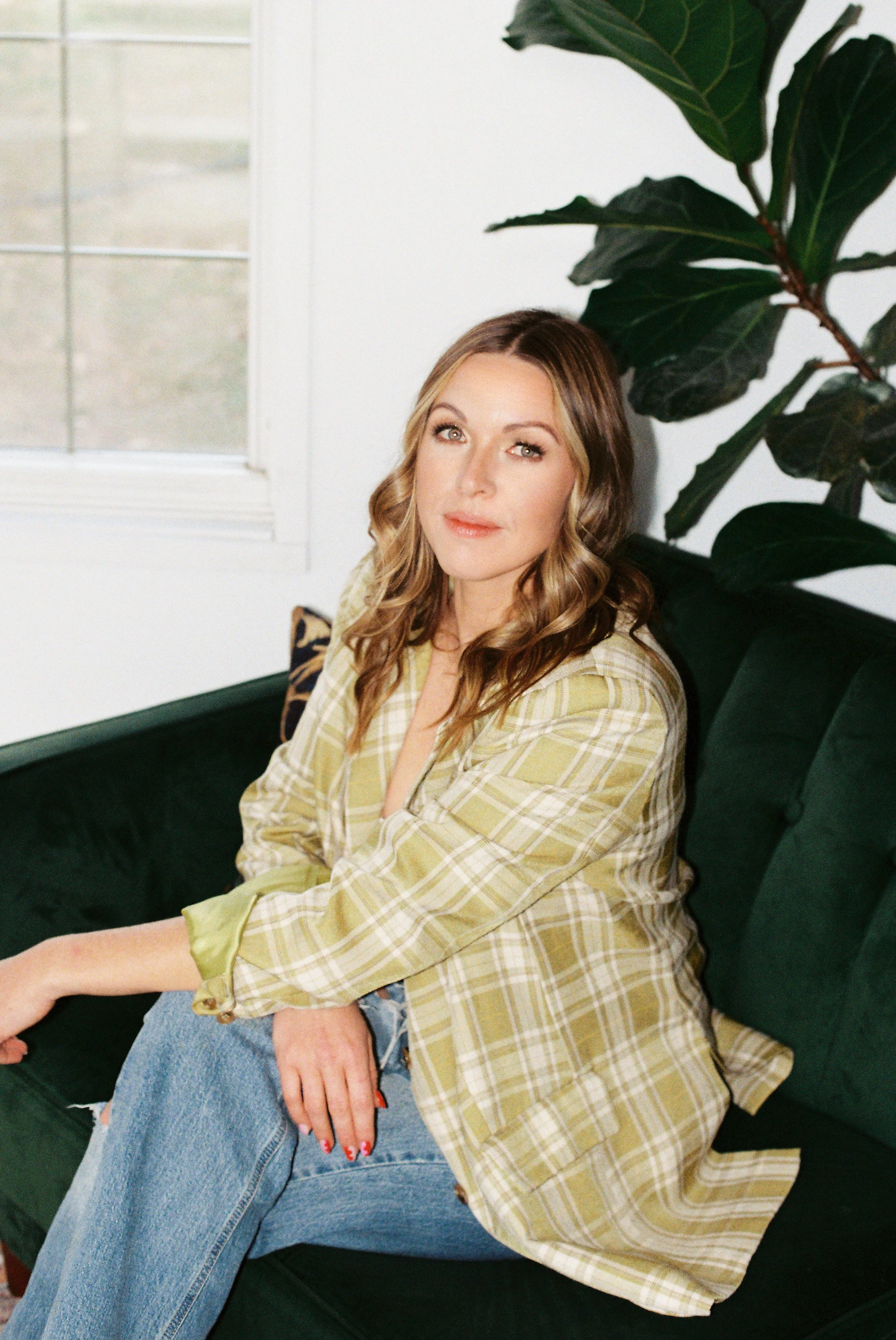 Gabby Pinkerton seated on a green velvet couch in a plaid jacket, smiling